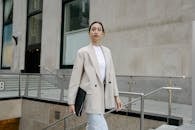 Confident Asian female entrepreneur in stylish outfit and with folder walking in city street and looking away