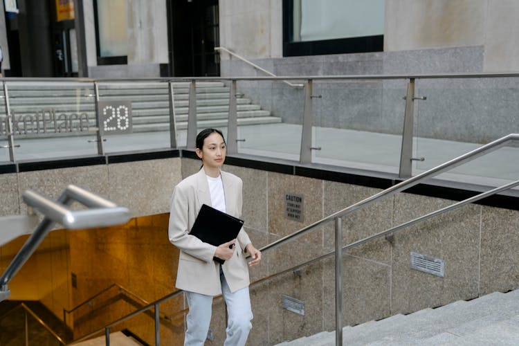 Ethnic Businesswoman With Folder Walking Upstairs In City