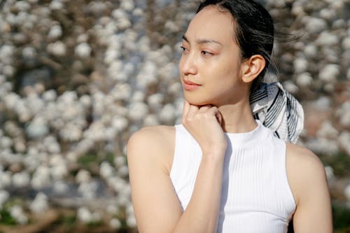 Young contemplative ethnic female in white clothes looking away on windy day on blurred background