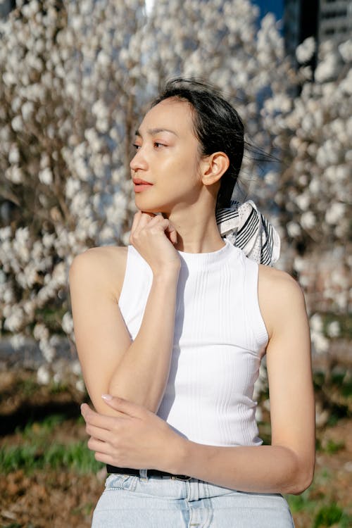 Dreamy young gentle Asian female touching neck while looking away on windy day in city