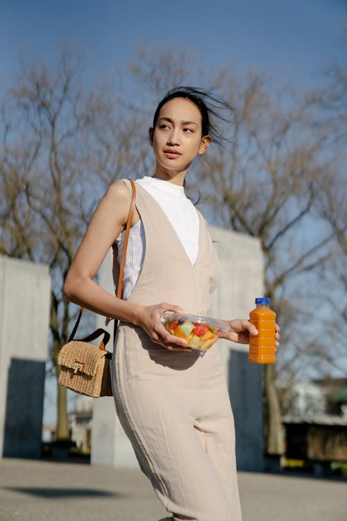 Ethnic woman with fruit salad and beverage walking in town