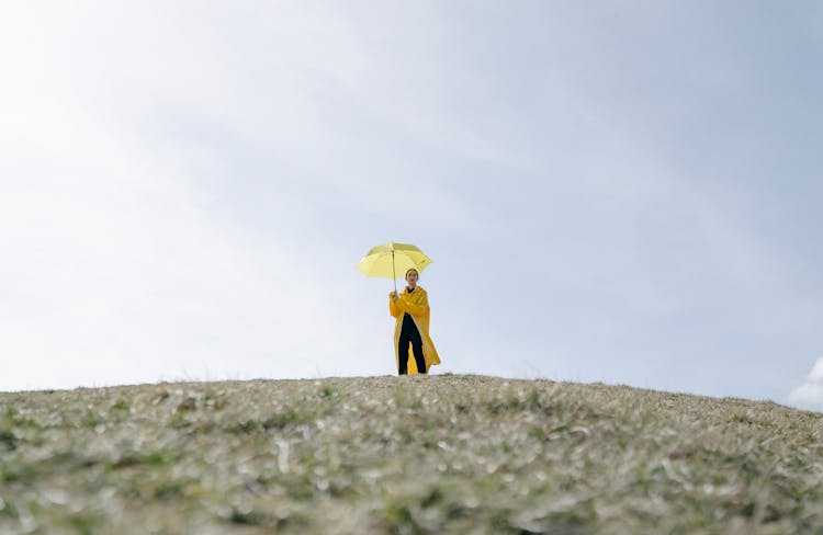 Woman With Yellow Umbrella On Land Under Cloudy Sky