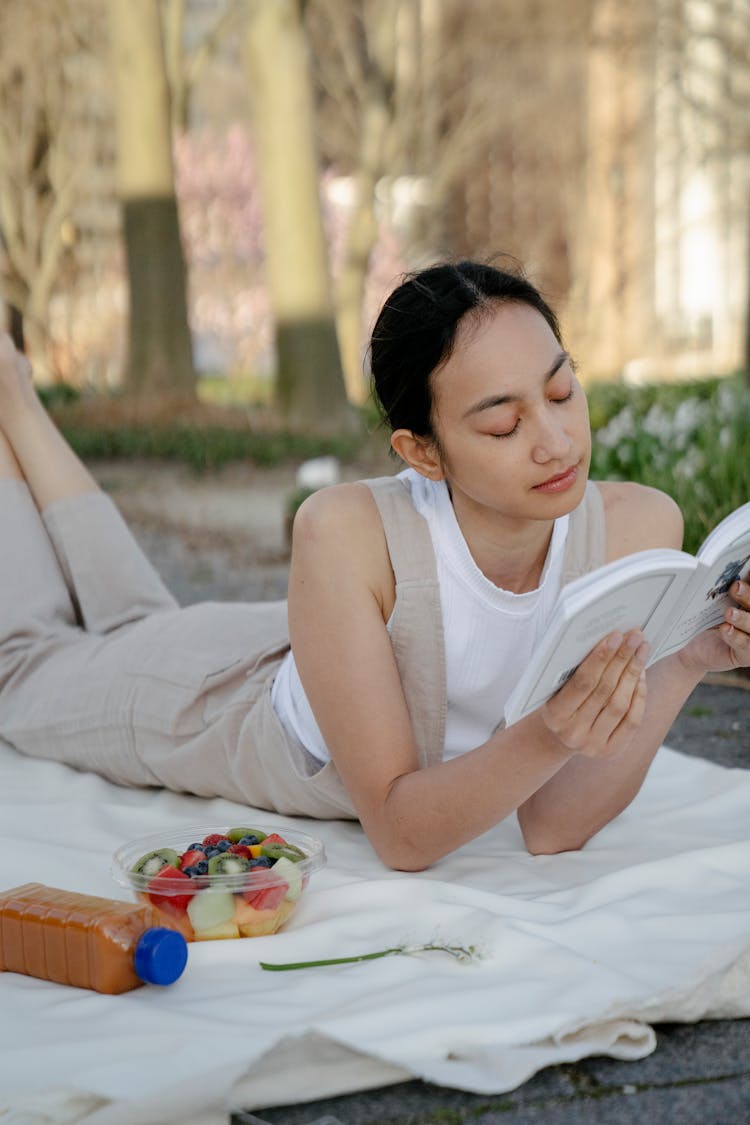 Asian Woman With Book And Fruit Salad Resting In Park