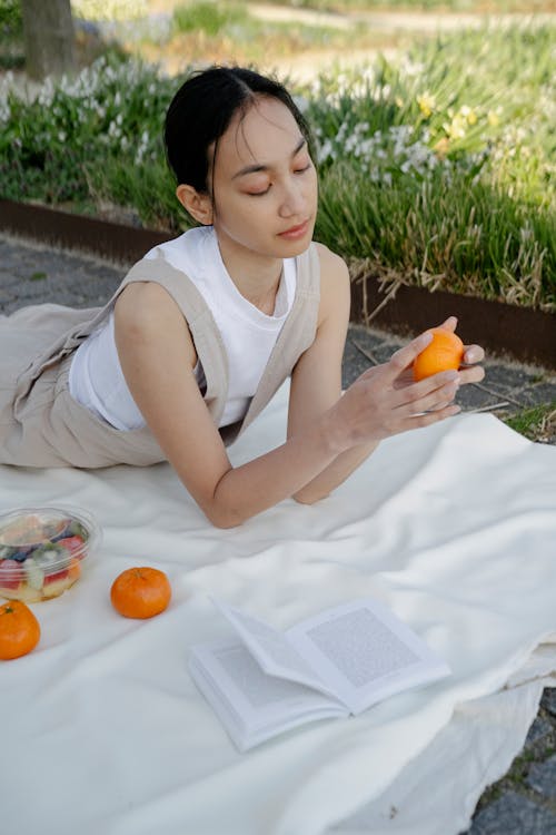 Asian woman with fresh tangerine on fabric in park