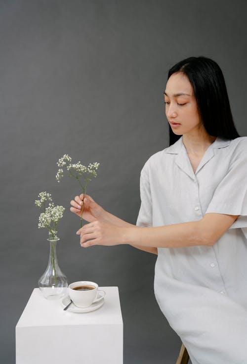 Asian woman with blooming flower sprig above coffee