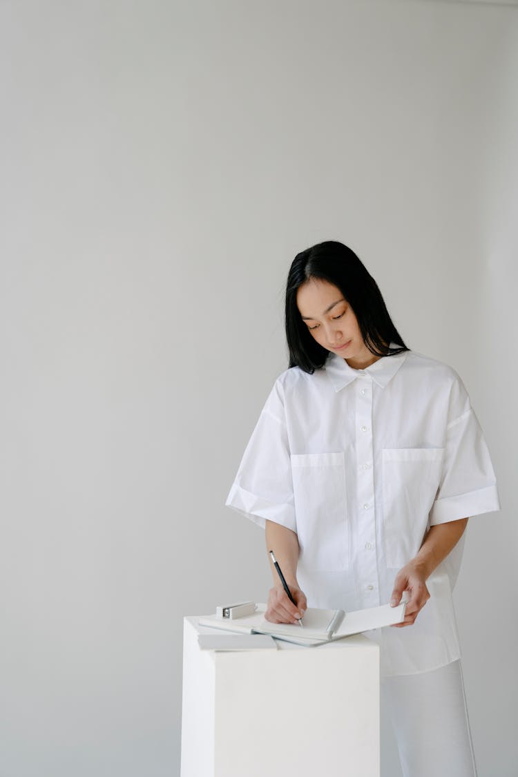 Asian Woman Writing In Diary On Light Background