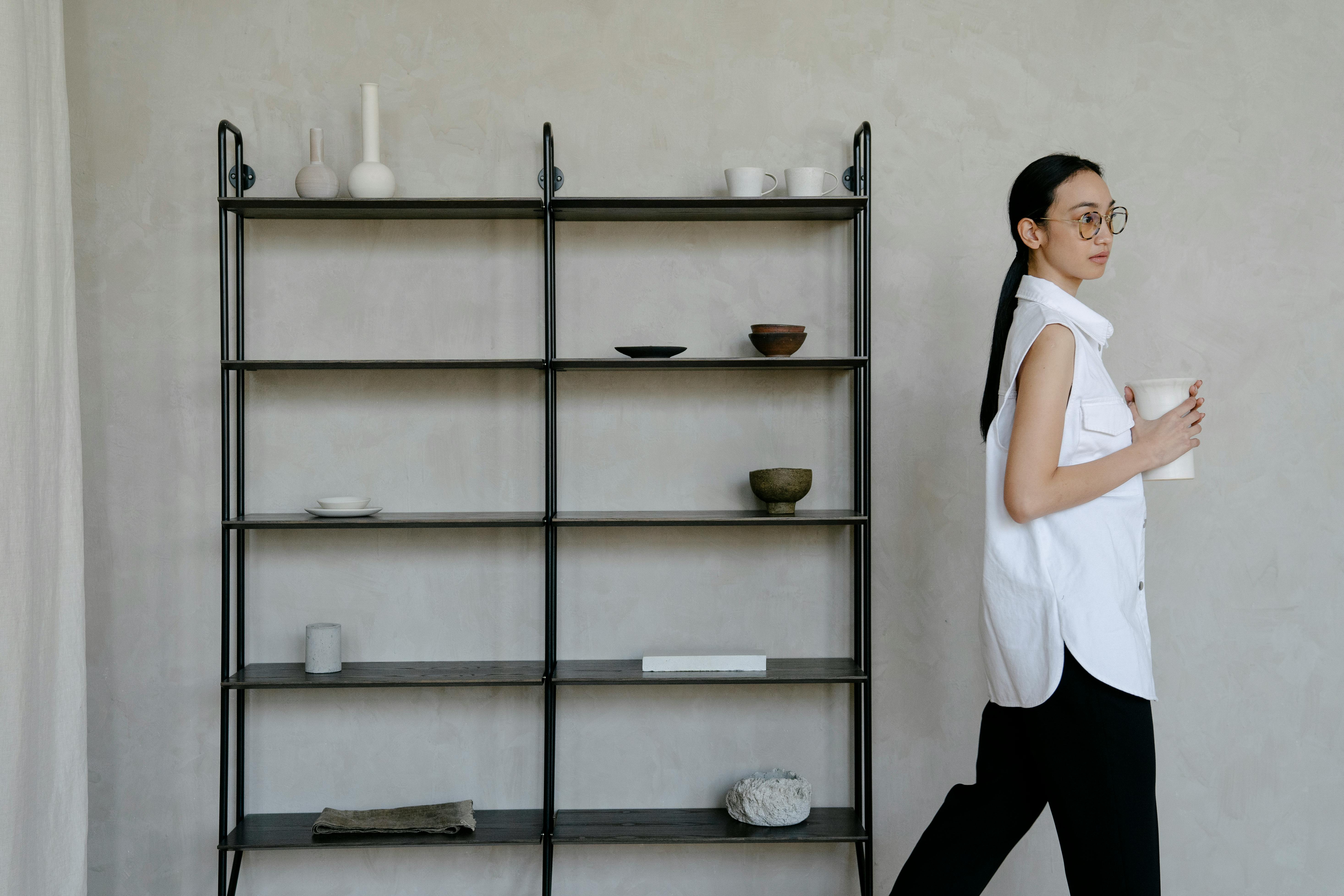 trendy ethnic woman walking in room near shelf with assorted decorative elements