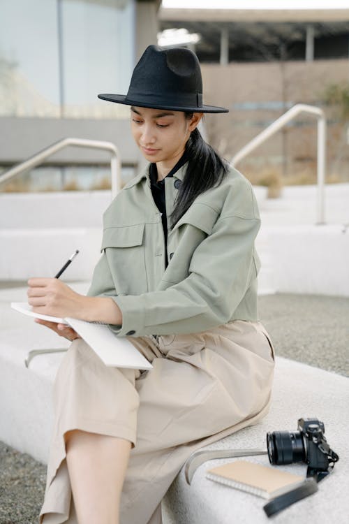 Trendy young Asian female millennial taking notes in diary in park