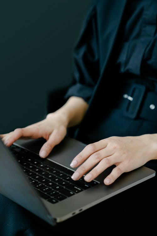 Free Crop unrecognizable female freelancer in black clothes typing on netbook keyboard while working on project Stock Photo