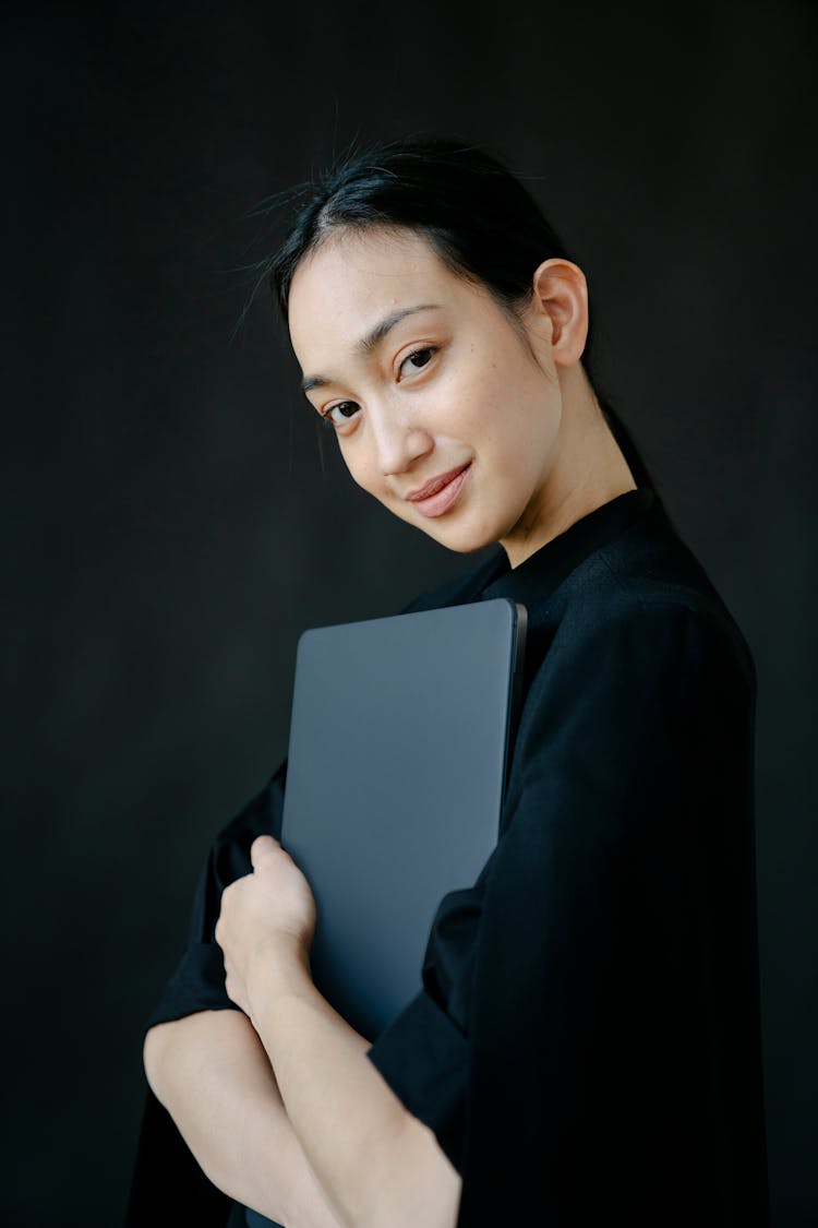 Smiling Asian Woman Hugging Laptop In Studio