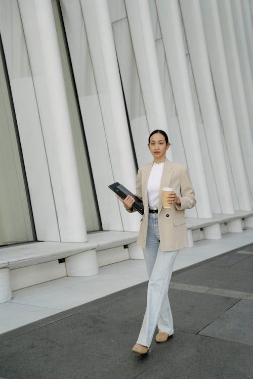 Ethnic woman carrying laptop with folder and cup of coffee