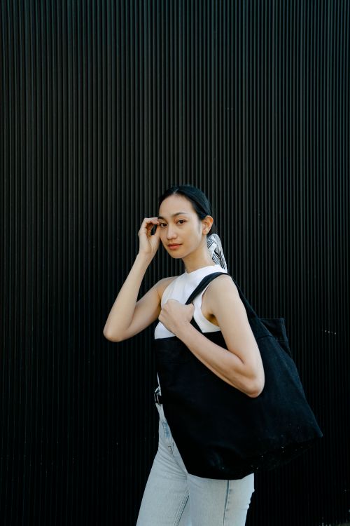 Free Gentle ethnic female wearing casual clothes standing with shopping bag and touching hair while looking at camera Stock Photo