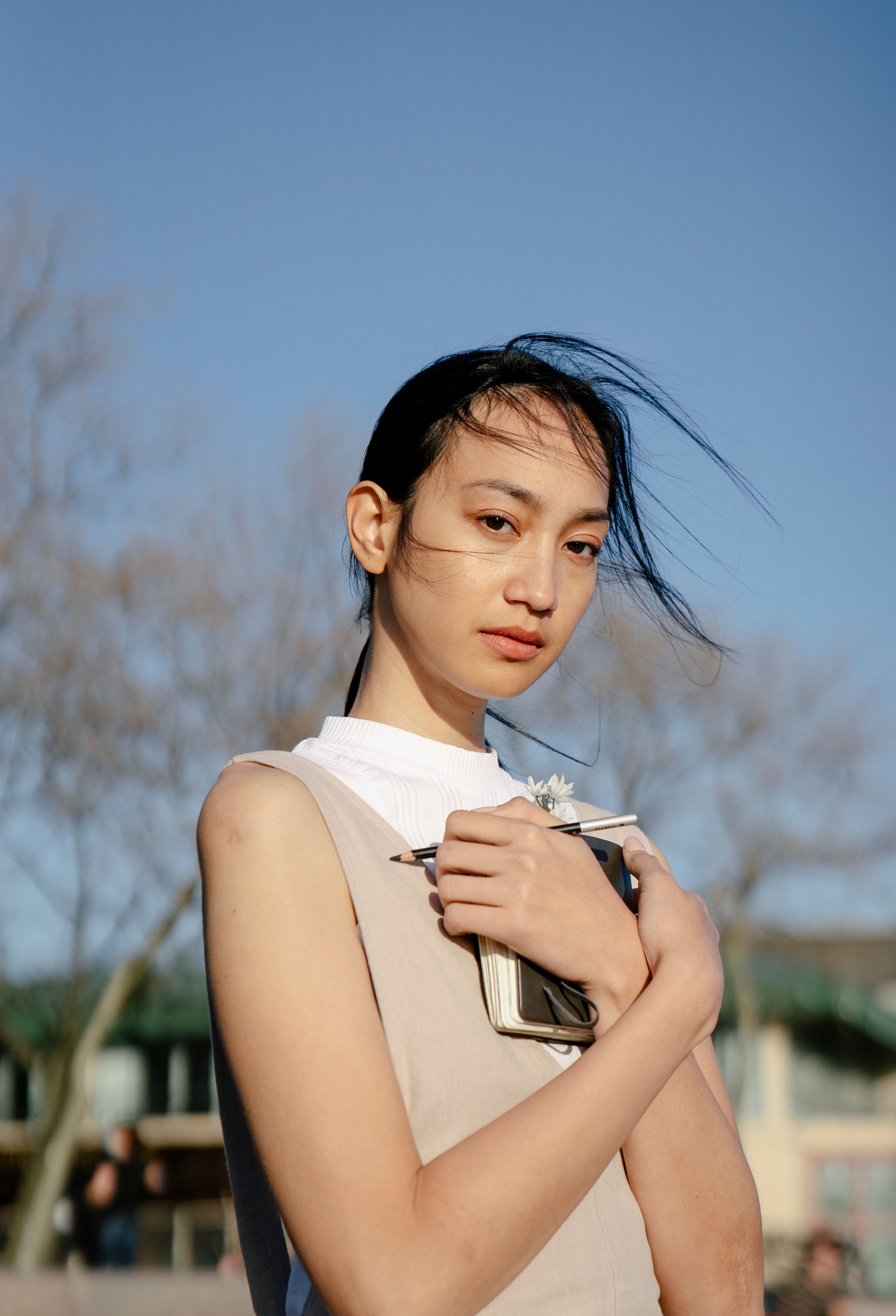 Asian woman holding a notebook outdoors in spring with a thoughtful expression.