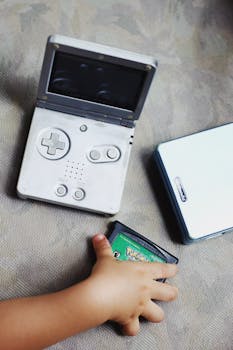 A child's hand holds a vintage Gameboy cartridge next to an open Gameboy SP console.