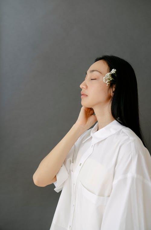 Free Calm young ethnic lady touching neck with closed eyes in gray studio Stock Photo