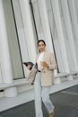 Stylish Asian businesswoman with laptop and takeaway coffee in city