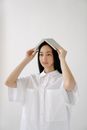 Smart young ethnic female bachelor in white shirt with diary on head looking forward on light background