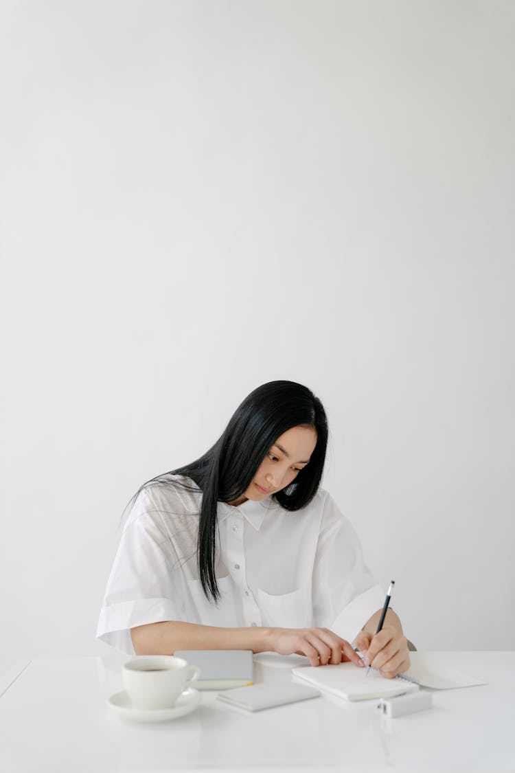 Focused Asian Employee Writing In Diary At Office Desk