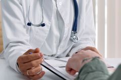A doctor in a white coat consulting a patient at a table with medical documents.