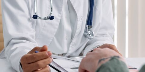 A doctor in a white coat consulting a patient at a table with medical documents.