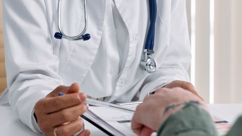 A doctor in a white coat consulting a patient at a table with medical documents.