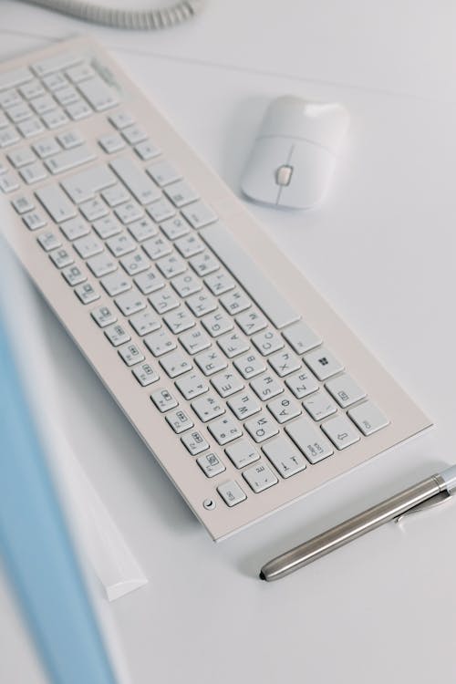 A White Keyboard Near a Silver Pen
