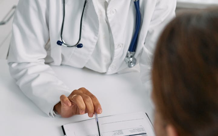 A doctor consulting with a patient in a medical clinic setting, reviewing a medical chart for diagnosis.