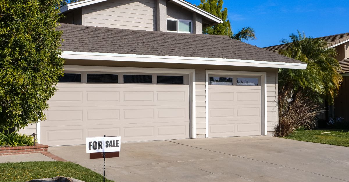 Modern residential house with a two-car garage and a for sale sign.
