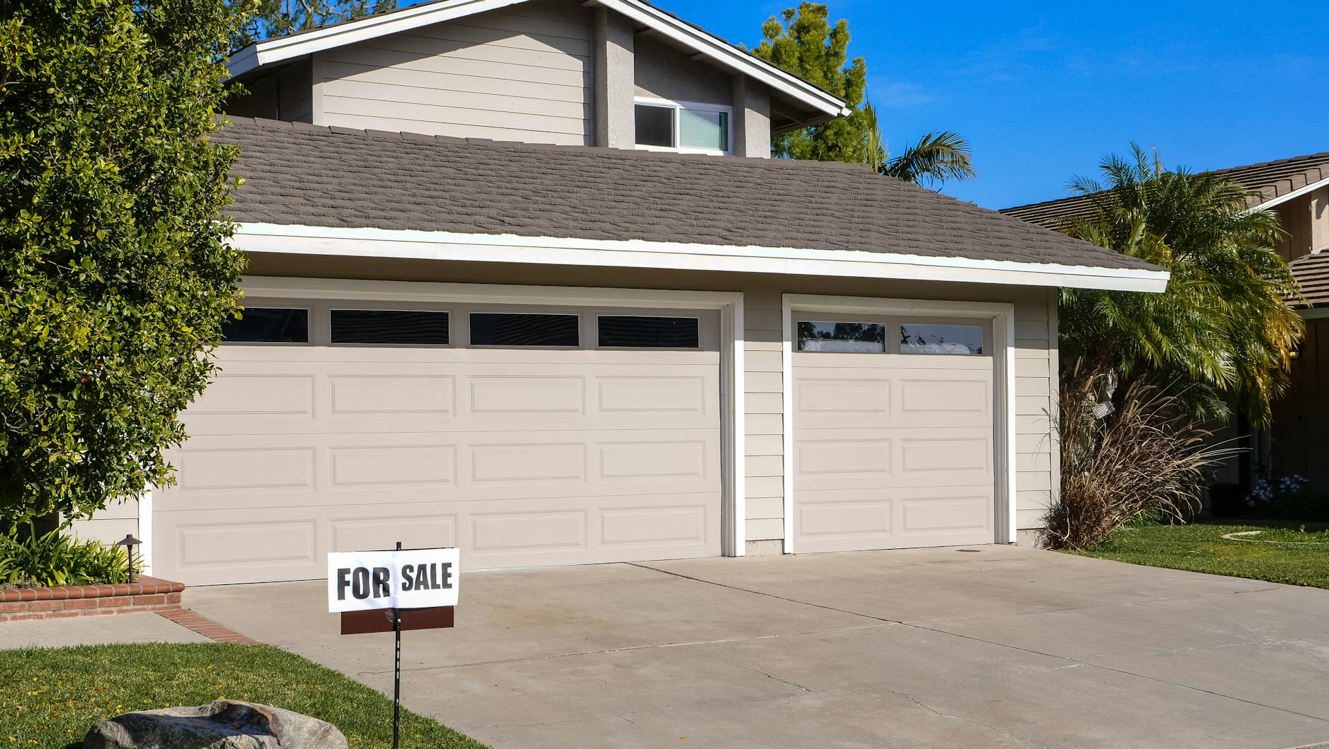 Modern residential house with a two-car garage and a for sale sign.