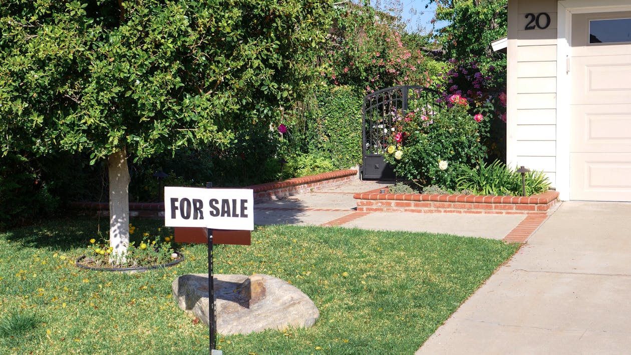 Free Front view of a house with a garden and 'For Sale' sign in bright daylight. Stock Photo