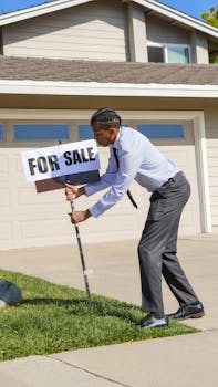 Professional real estate agent placing a for sale sign in front of a house on a sunny day.