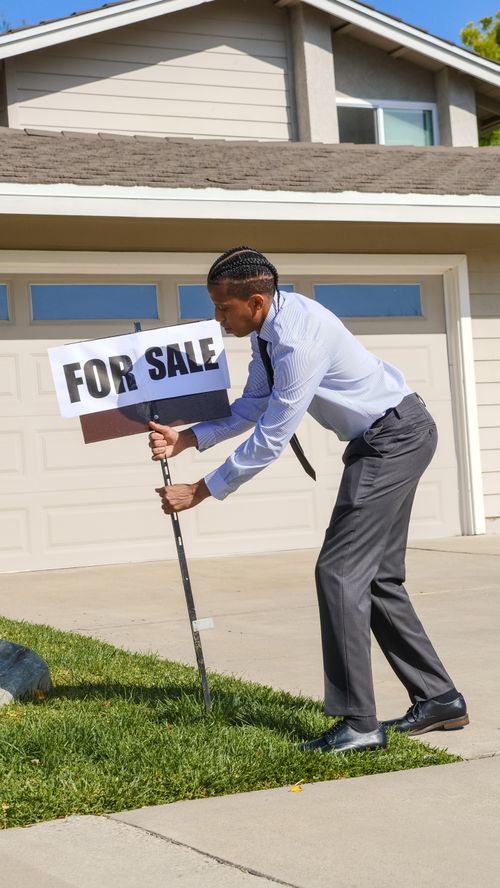 Free Professional real estate agent placing a for sale sign in front of a house on a sunny day. Stock Photo