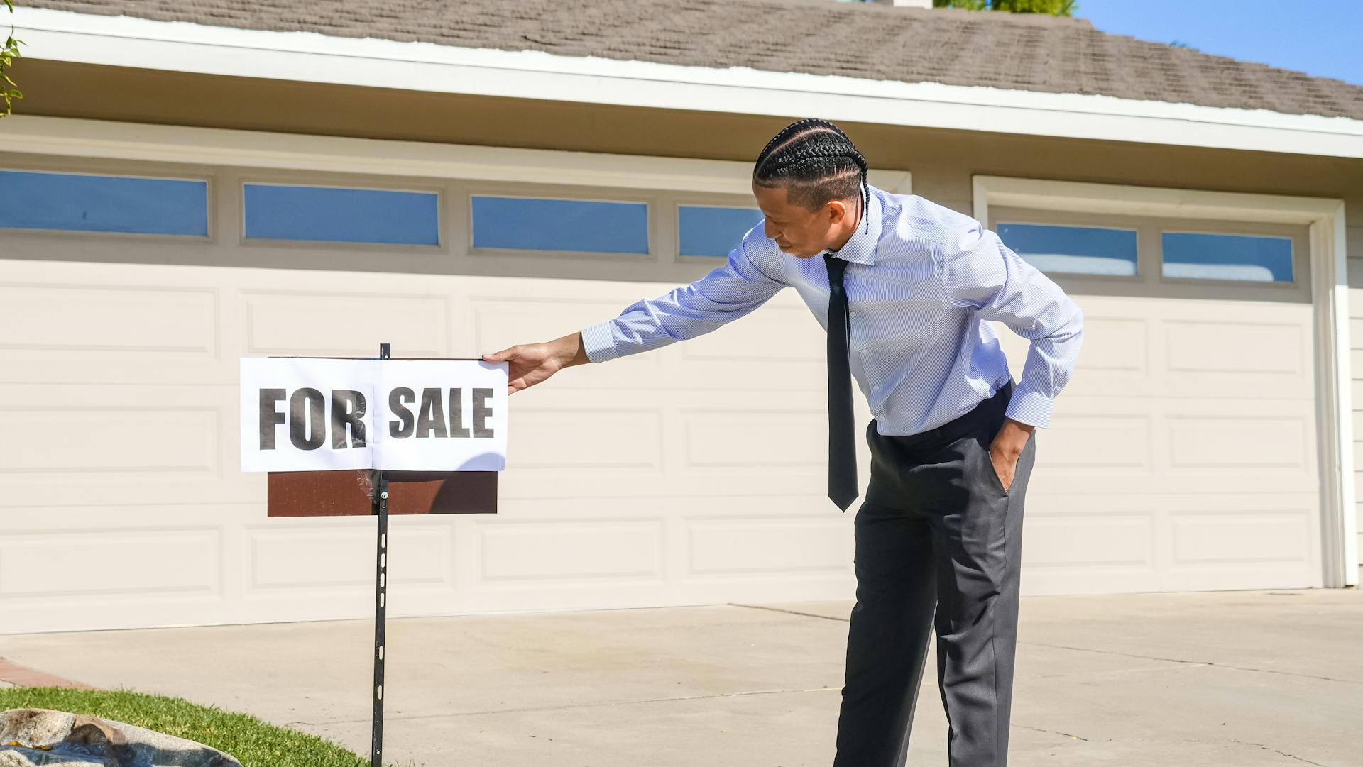 Professional real estate agent setting up a for sale sign outside a house.