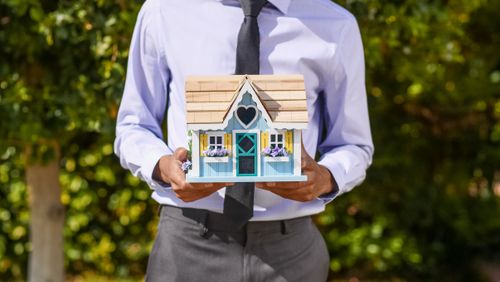 Free A business professional holds a decorative miniature house, symbolizing real estate investment. Stock Photo