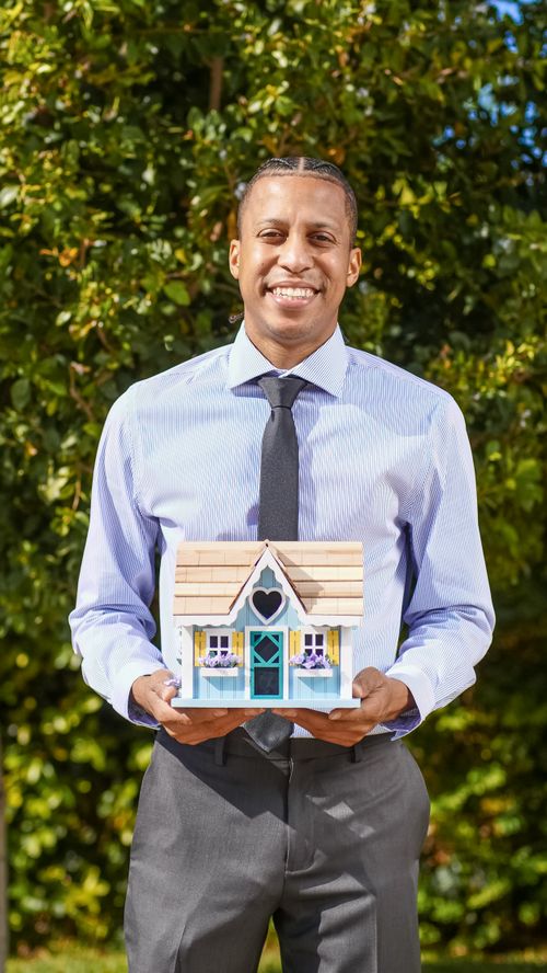 Free Smiling real estate agent holding a model house in an outdoor setting. Stock Photo