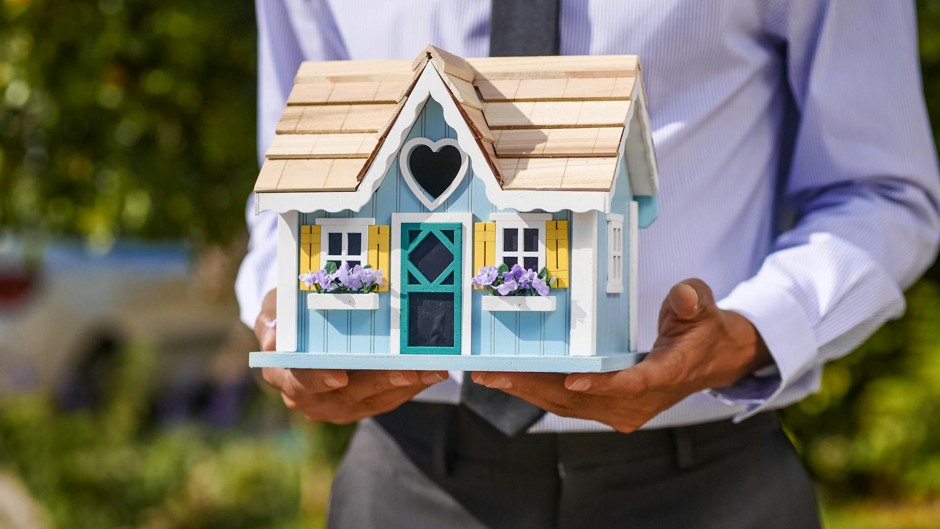 A businessman holds a detailed, colorful miniature house model. Ideal for concepts of real estate and property investment.