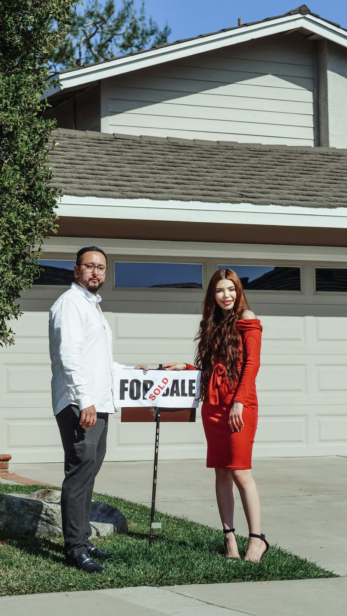 Happy couple in front of a middle class home with a sold sign on the lawn