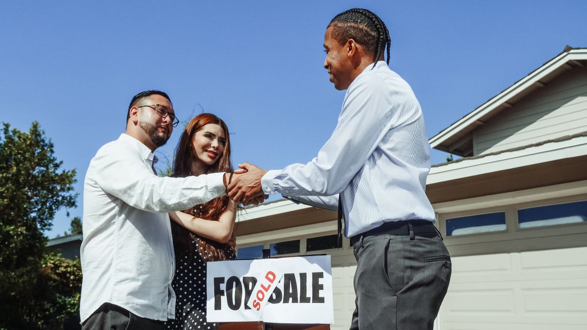 Agent commercial indépendant serrant la main de ses clients devant leur nouvelle maison