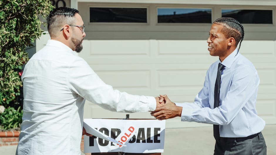 Two men shaking hands in front of a sold house sign, sealing a real estate transaction.