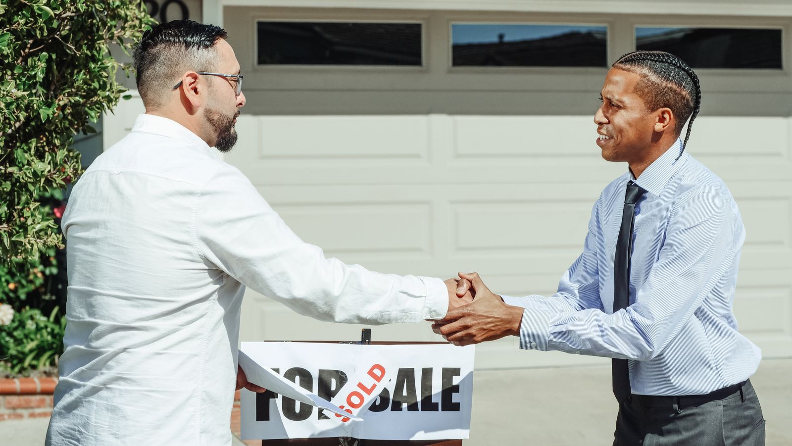 Real estate agent shaking a buyer's hand in front of a For Sale sign