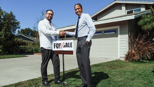 Two people shaking hands in front of a UK house, illustrating a pre-completion sub-sale transfer of rights under SDLT sub-sale relief
