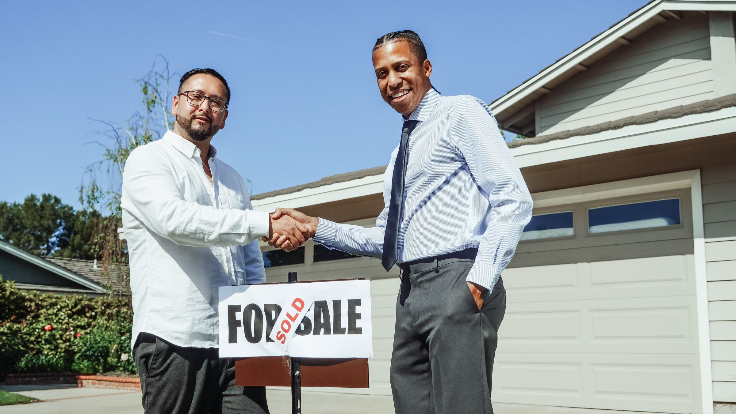 Two men shaking hands in front of a house after agreement