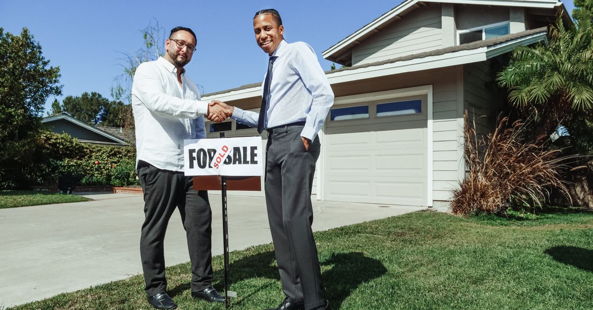 Two people shaking hands in front of a newly sold house, with a