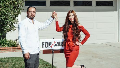 Free A joyful couple holding Sold sign in front of their new house, celebrating a home purchase. Stock Photo