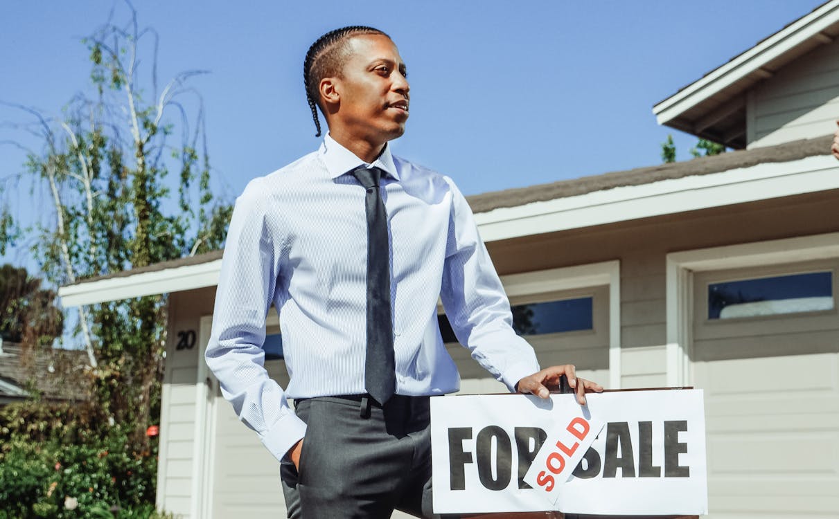 Man in Dress Shirt and Black Necktie Holding on a Sold Sign