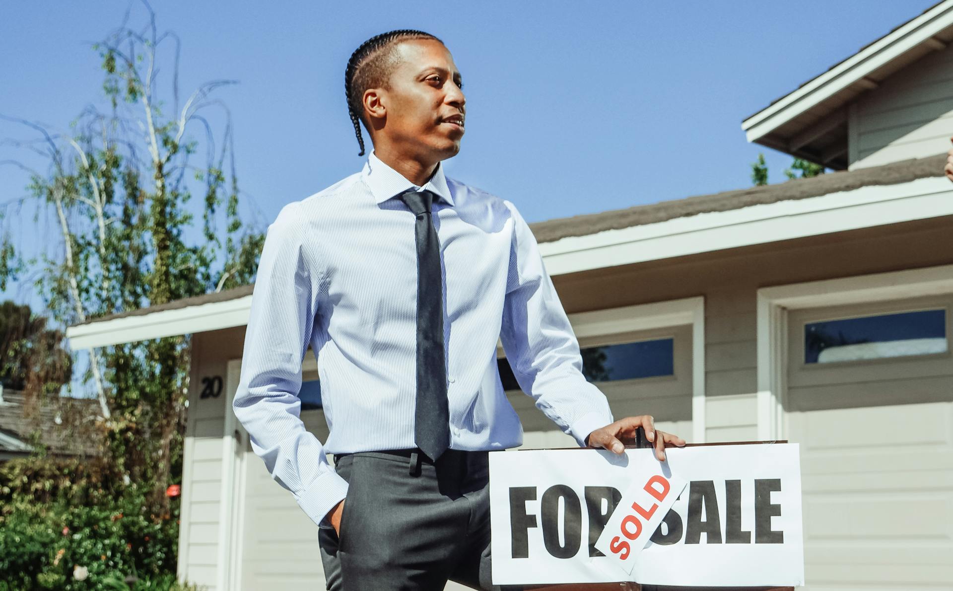 Real estate agent presenting a sold sign in front of a residential property.