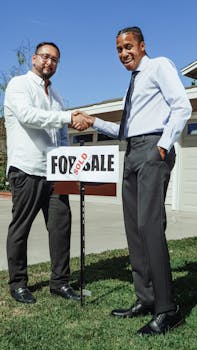 Two men shaking hands in front of a house with a sold sign, marking a successful real estate deal.