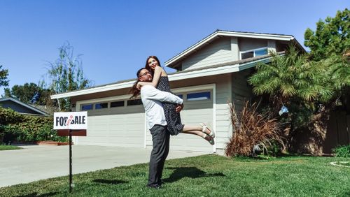 Free A joyful couple celebrating their new home purchase in front of a house with a sold sign. Stock Photo