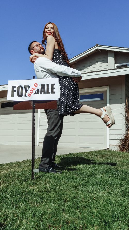 Free A joyful couple celebrates buying their new house with a 'Sold' sign. Stock Photo