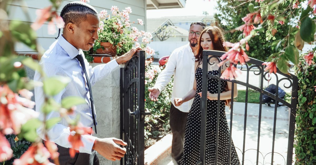 Realtor welcoming a couple to a new house, showcasing the property gate and garden.